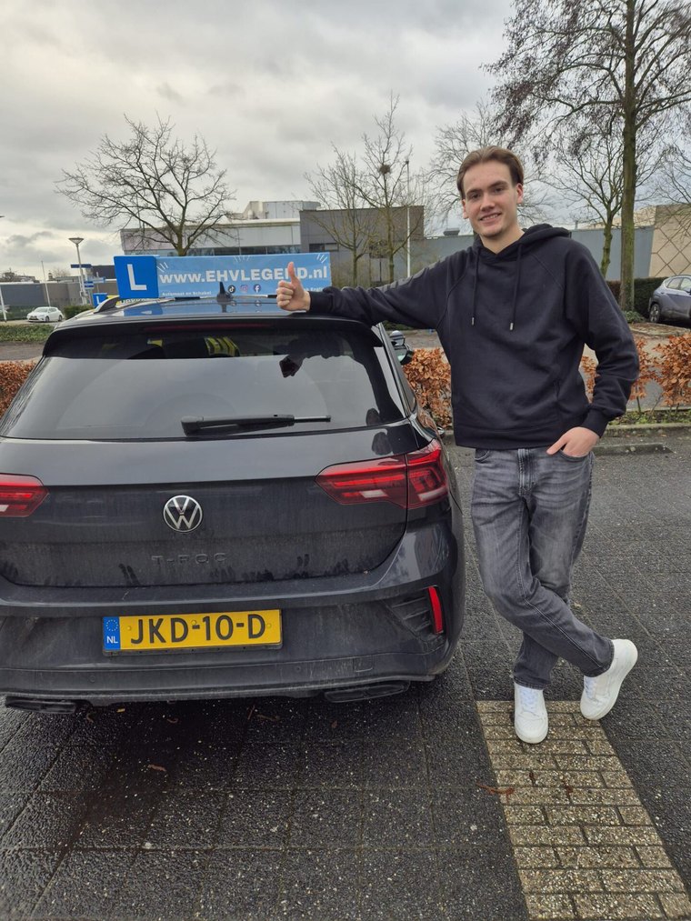 Geslaagde leerling met duim omhoog naast de lesauto van Rijschool EHVLegend