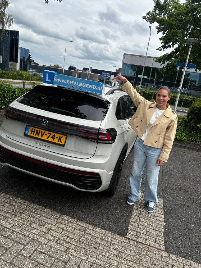 Geslaagde leerling juicht naast de witte lesauto van Rijschool EHVLegend