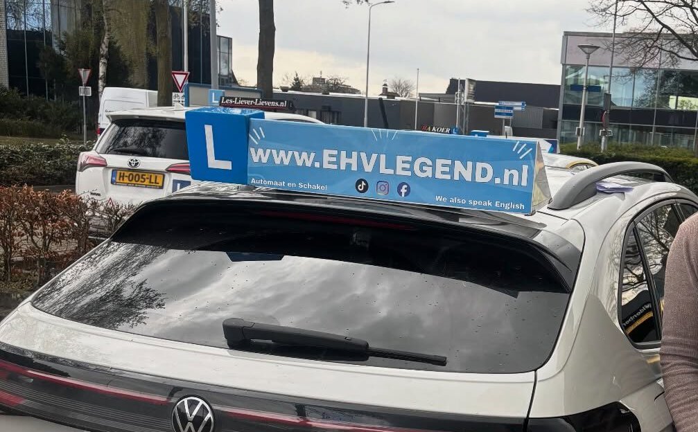 De witte lesauto van Rijschool EHVLegend met het blauwe L-bord en het EHVLEGEND.nl-dakbord